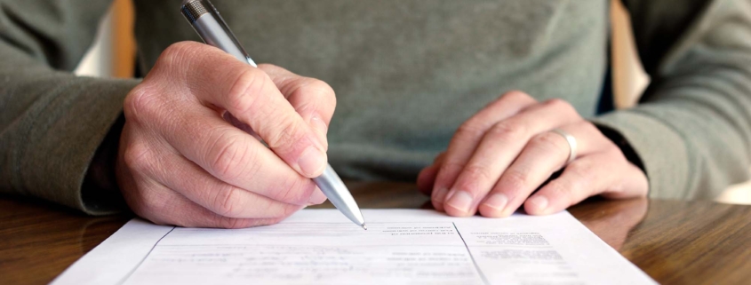 Man Writing on Paper with Pen on Table