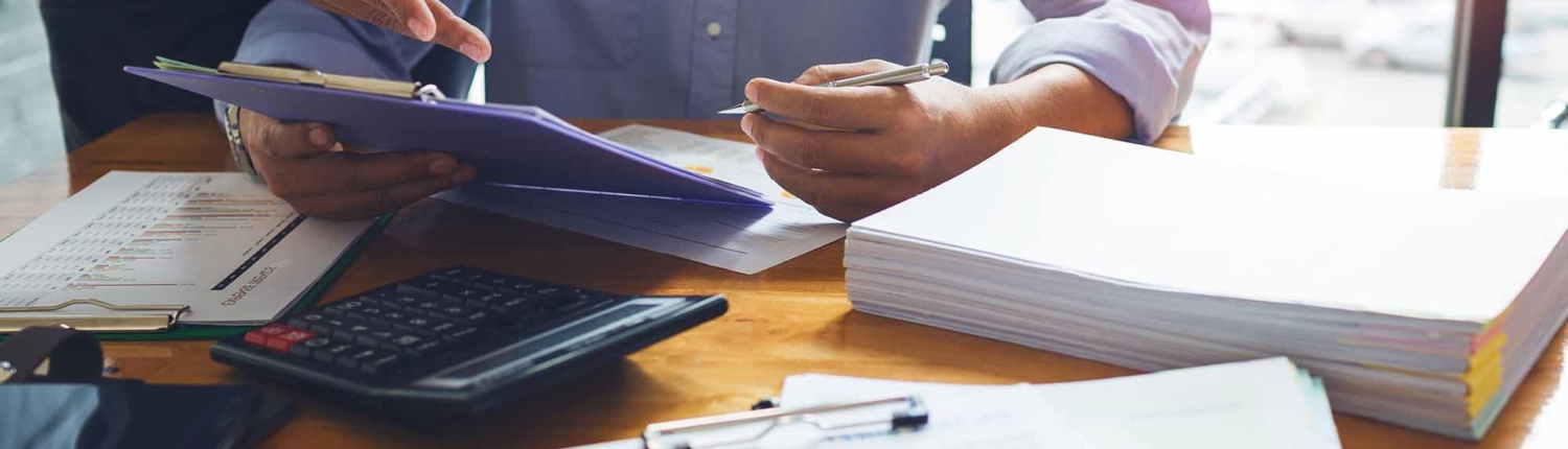 two people looking at a clipboard with papers and calculator on a table